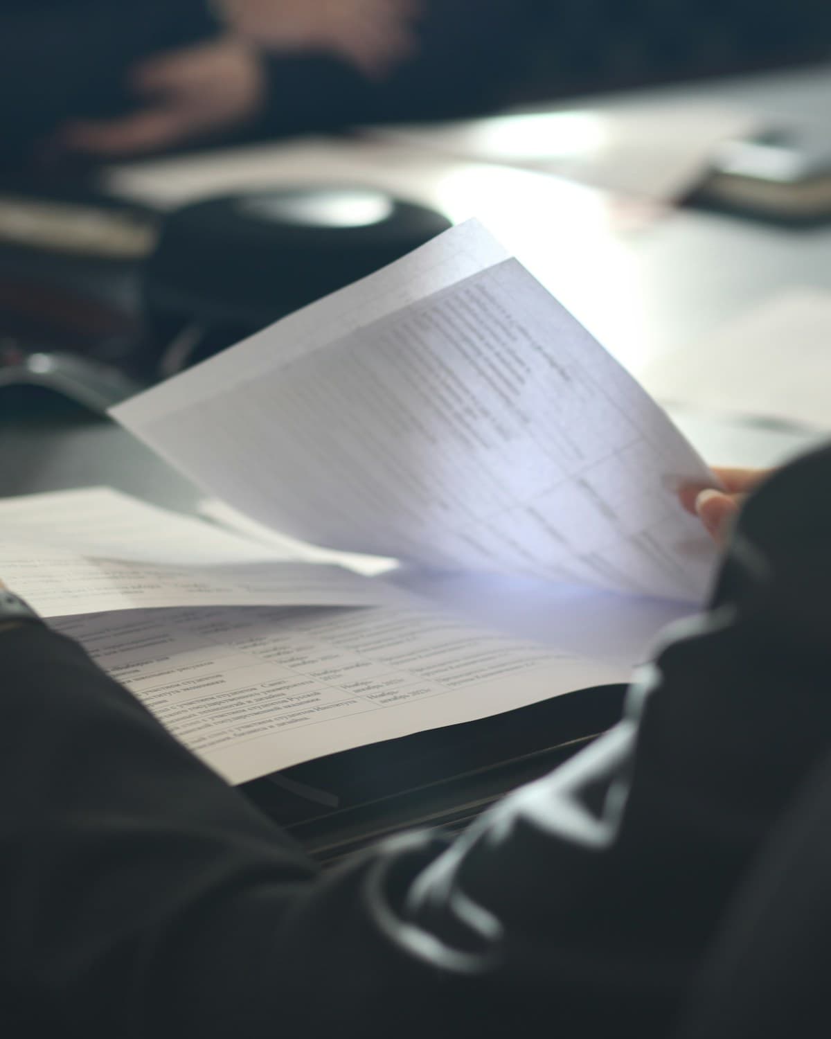 Persona con saco oscuro revisando documentos impresos con tablas sobre un escritorio.