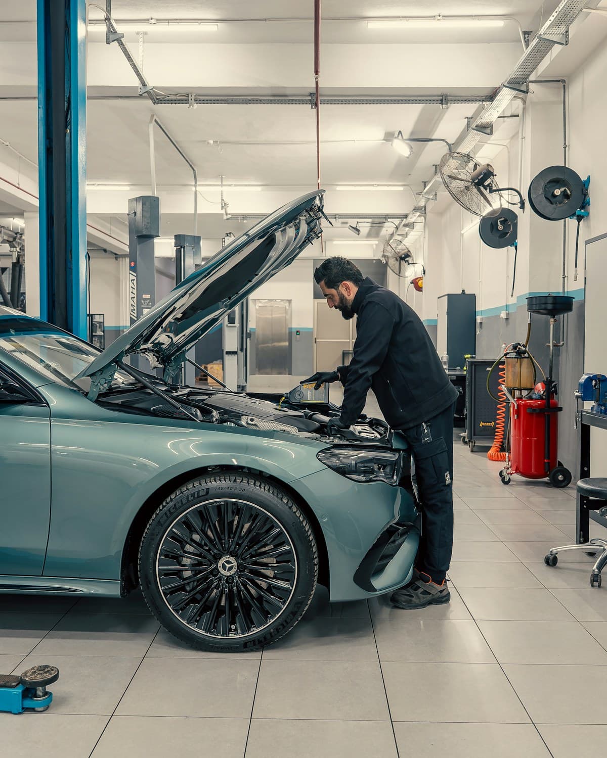 Persona con ropa oscura trabajando sobre el motor de un automóvil con el capó abierto en un taller.