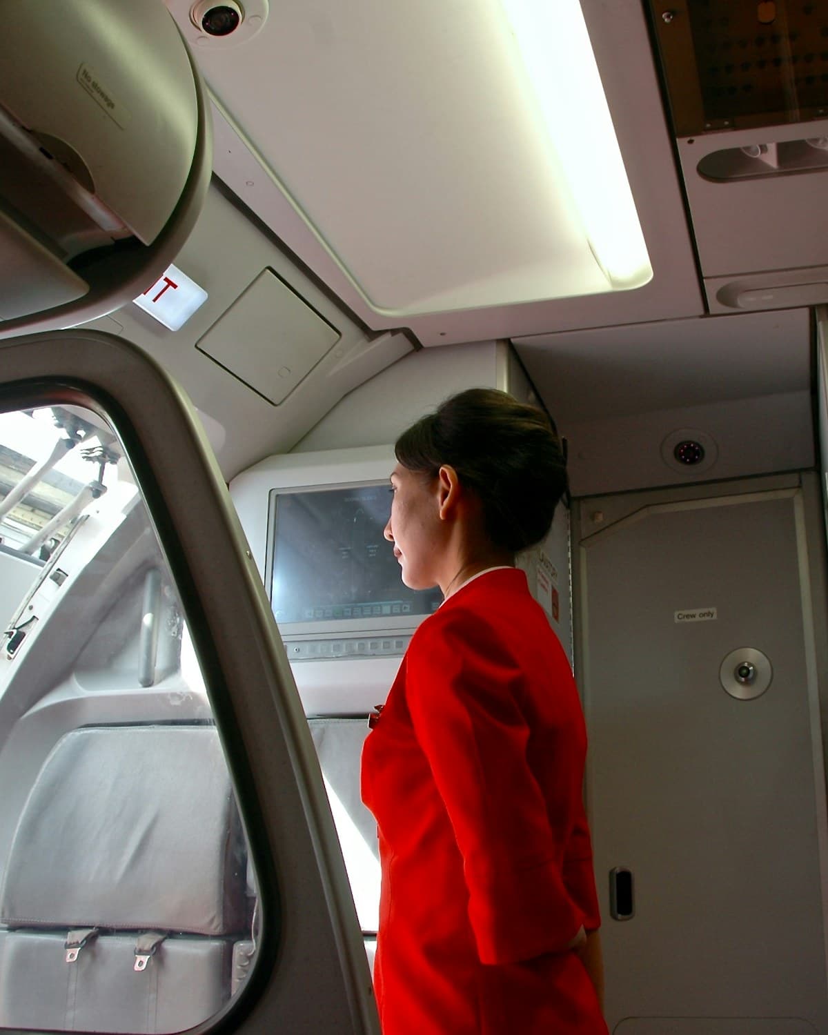 Tripulante de cabina con uniforme rojo junto a la puerta abierta de una aeronave.
