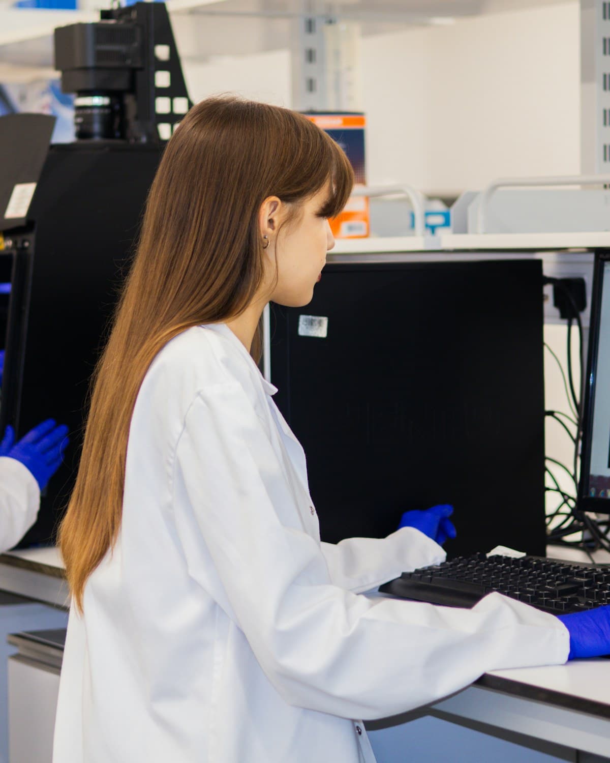 Profesional con guardapolvo y guantes azules trabajando frente a una computadora en un laboratorio.