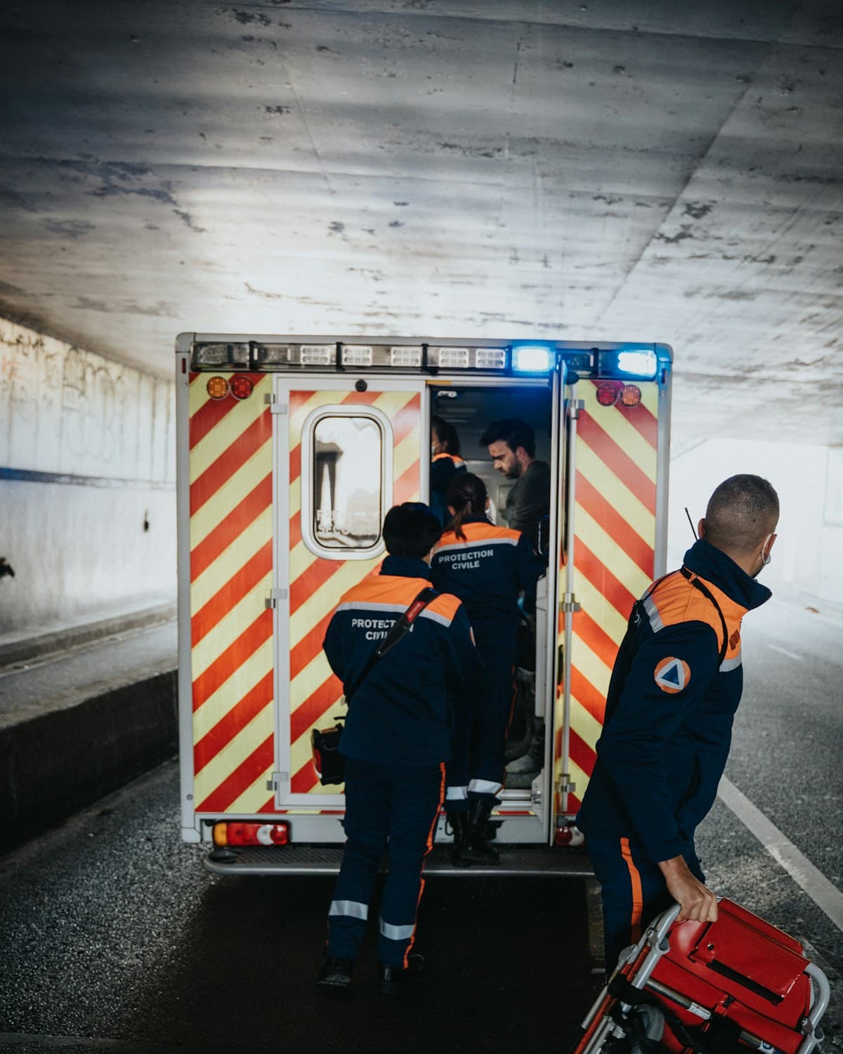 Tres integrantes de un equipo de emergencias junto a la parte trasera abierta de una ambulancia, con un maletín rojo en primer plano.