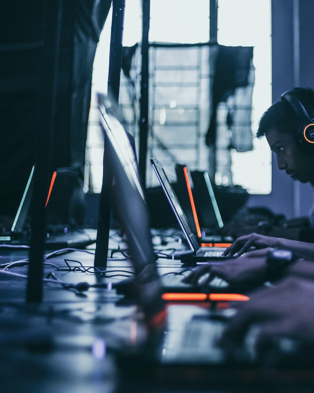 Personas con auriculares usan computadoras portátiles y monitores en una mesa iluminada con luces de colores.