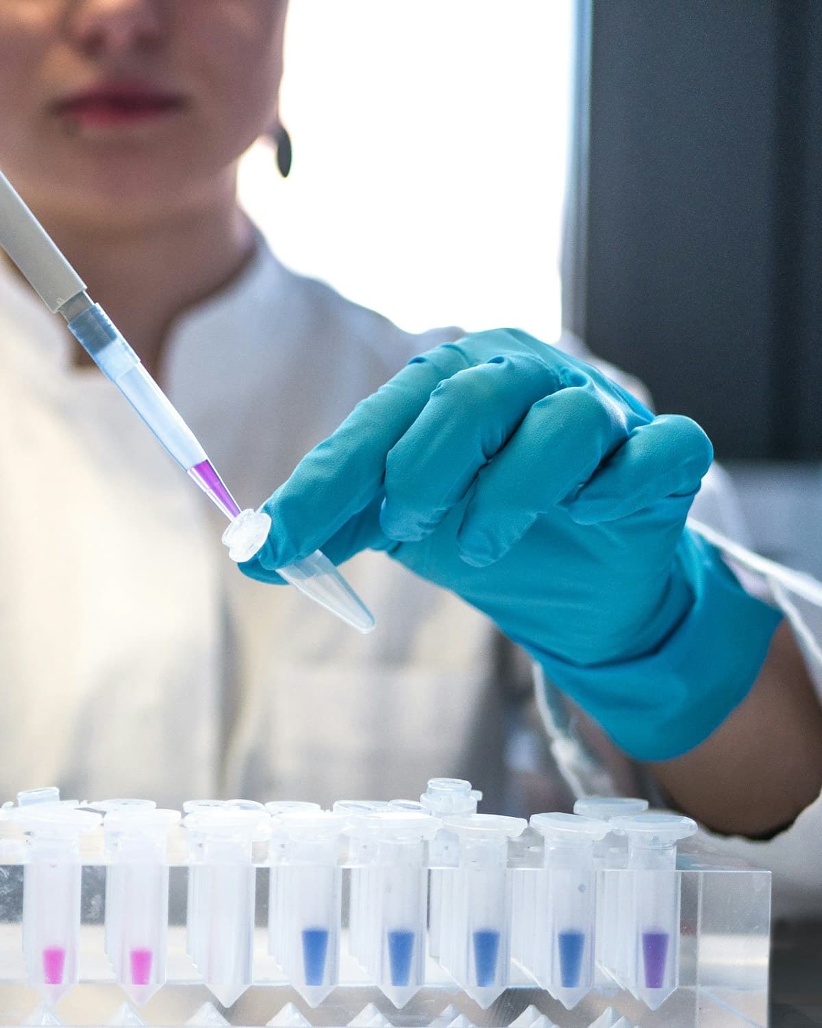 Persona con guantes azules usando una pipeta sobre tubos de ensayo con líquidos de colores en un laboratorio.
