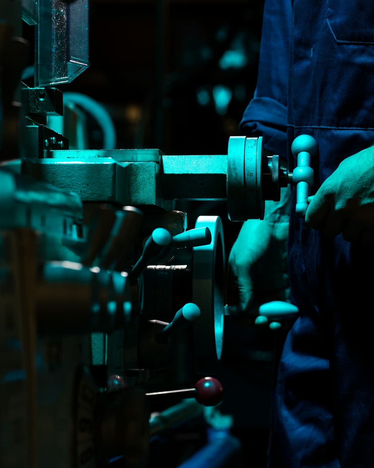Persona con mameluco azul operando los mandos de una máquina industrial en un taller.