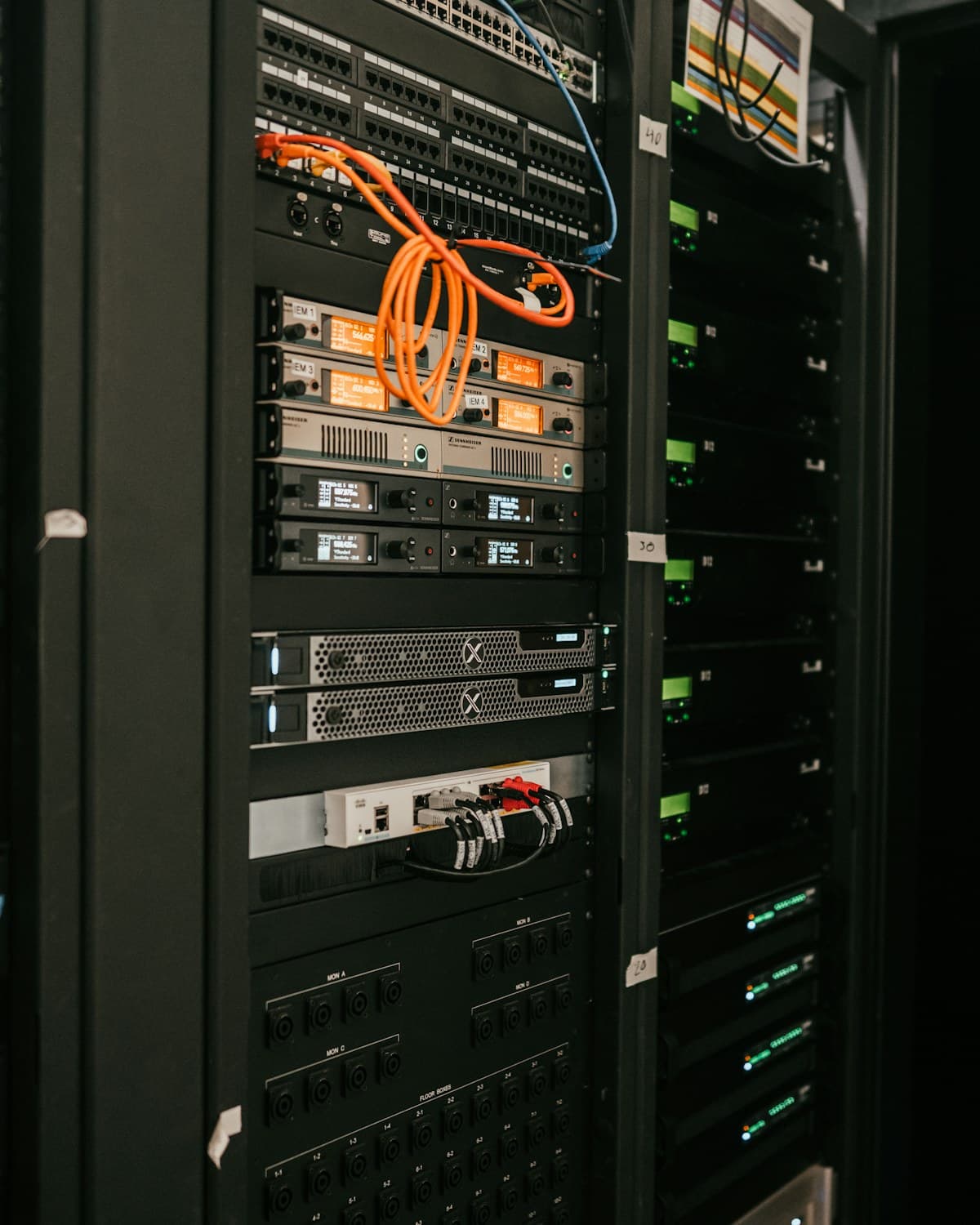Racks de servidores con paneles de conexión, equipos montados y cables naranjas y negros en una sala técnica.