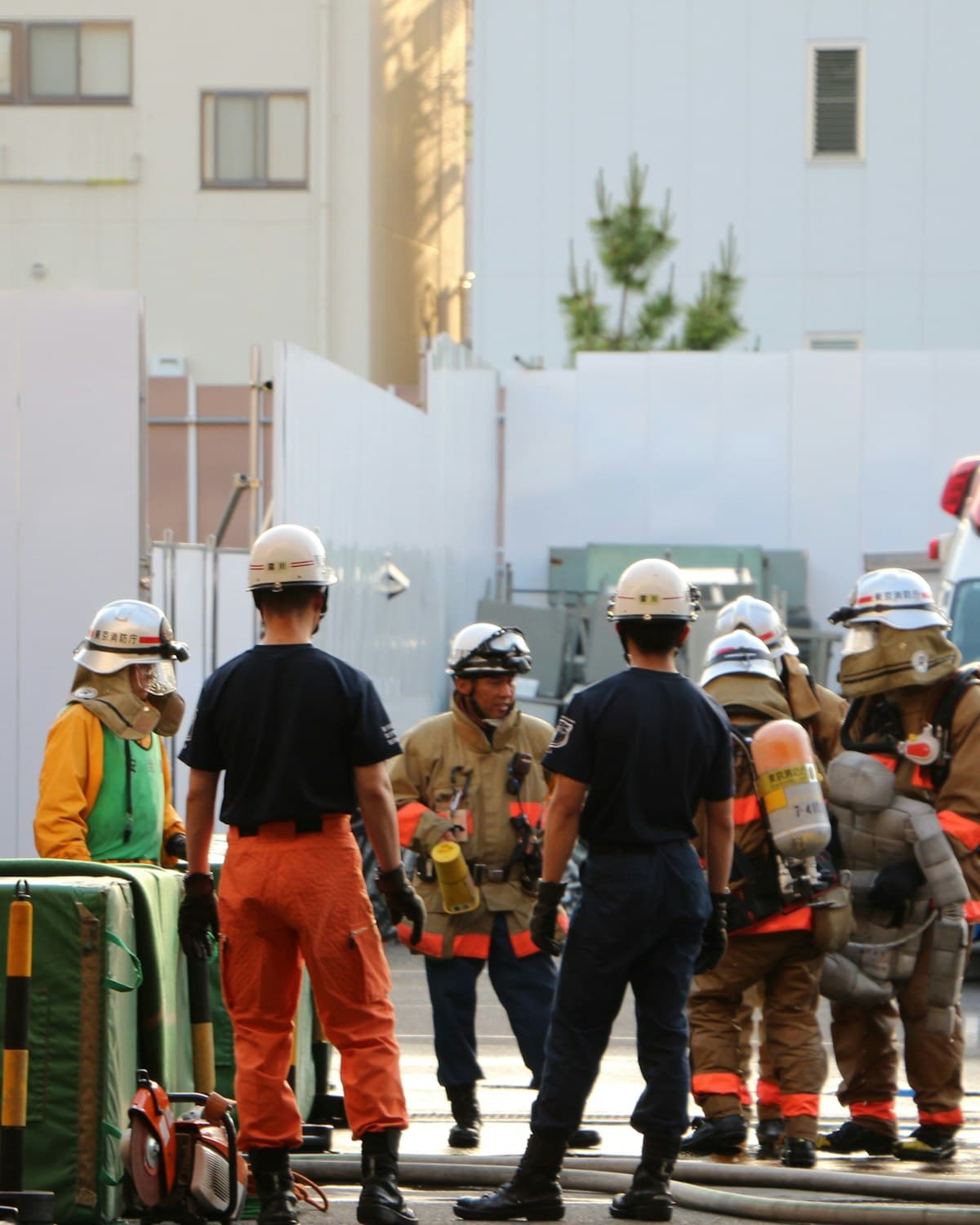Equipo de bomberos con cascos y equipos de respiración reunido en una calle junto a mangueras.