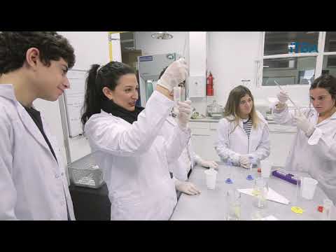 Estudiantes con guardapolvos realizan prácticas alrededor de una mesa de laboratorio
