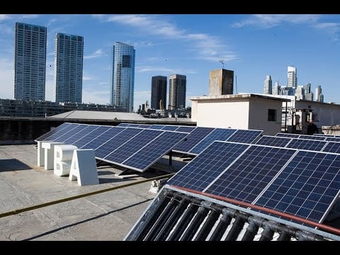 Paneles solares en una terraza con identificación del ITBA y edificios al fondo