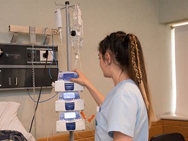 Estudiante con uniforme sanitario opera equipamiento de simulación clínica junto a una cama.