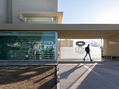 Acceso exterior del Instituto Universitario de Ciencias Biomédicas de Córdoba, con fachada vidriada y cartel institucional.