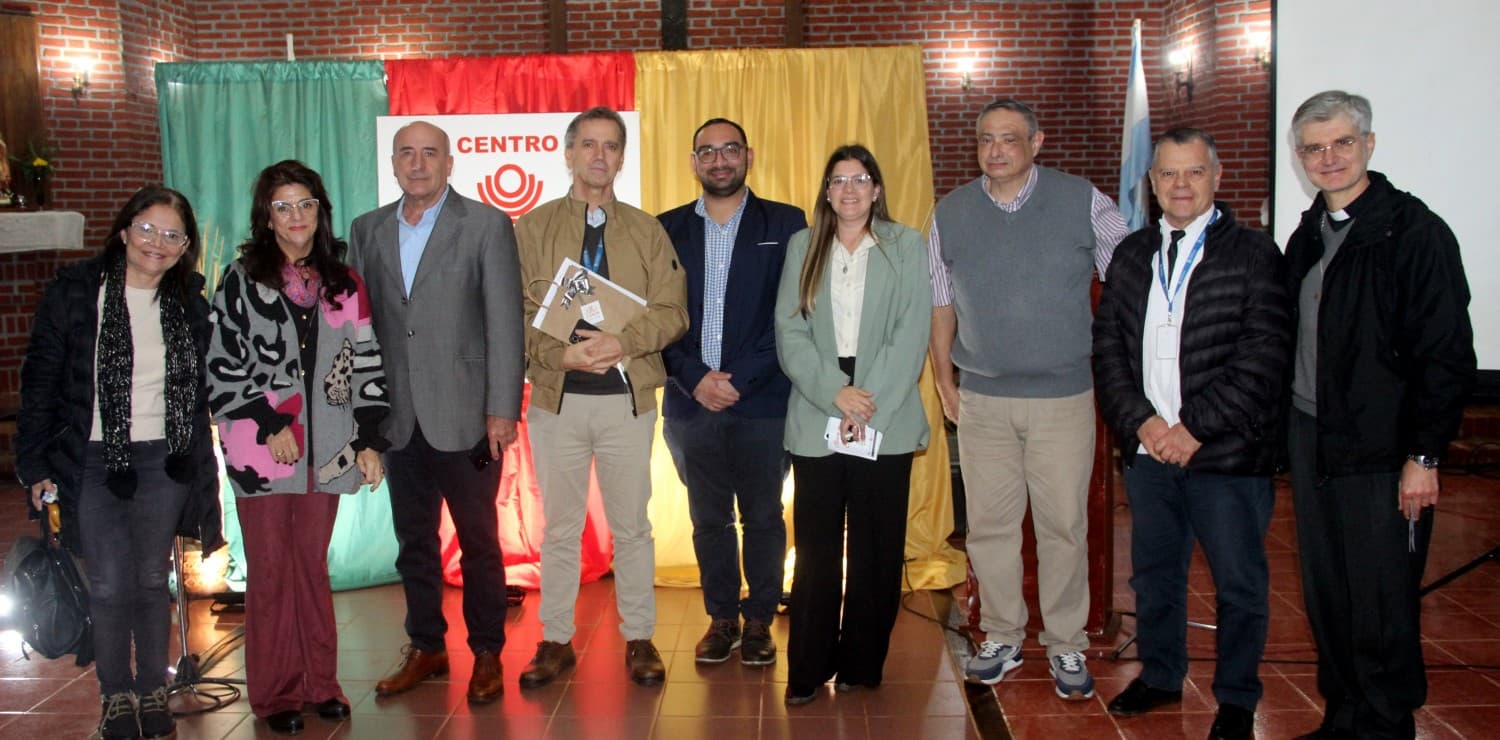 Grupo de personas reunidas en un salón con pared de ladrillo y pantalla de fondo
