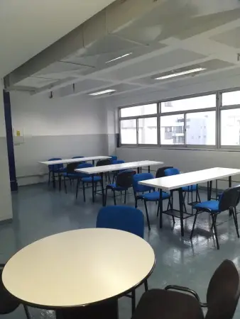 Sala de estudio con mesas, sillas azules y grandes ventanales.