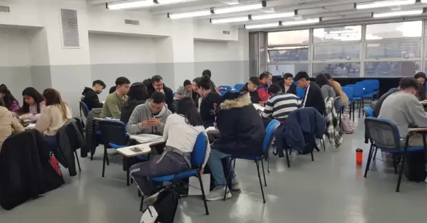 Estudiantes sentados en mesas durante una actividad de clase en un aula amplia.