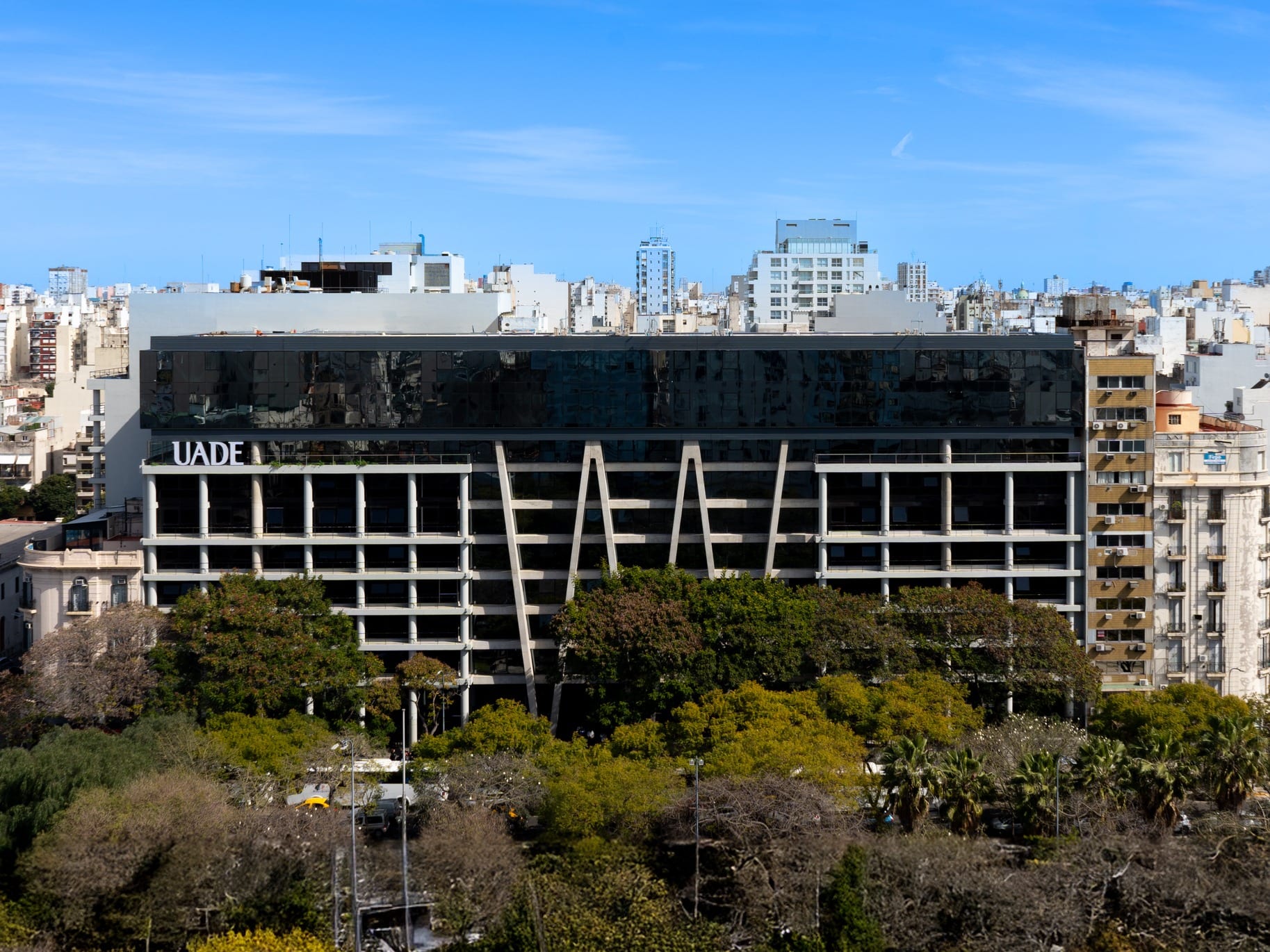 Vista aérea de un edificio de UADE con fachada acristalada frente a una zona arbolada.