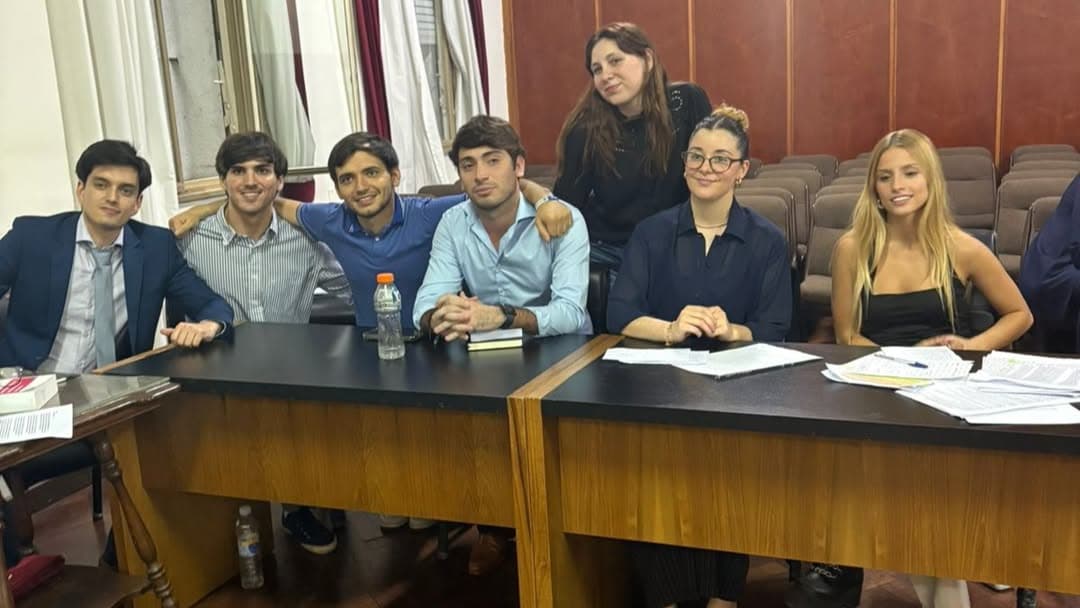 Grupo de estudiantes sentado alrededor de mesas con apuntes en una sala de audiencias.