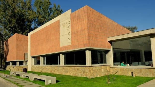 Edificio de ladrillo de la biblioteca, con ventanales, césped y bancos en el exterior.
