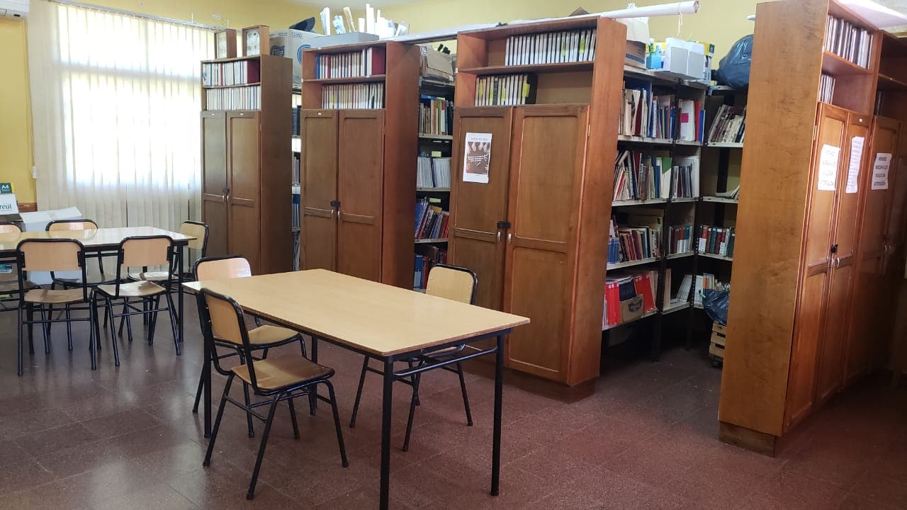 Sala de biblioteca con estanterías de libros, mesas y sillas para lectura.