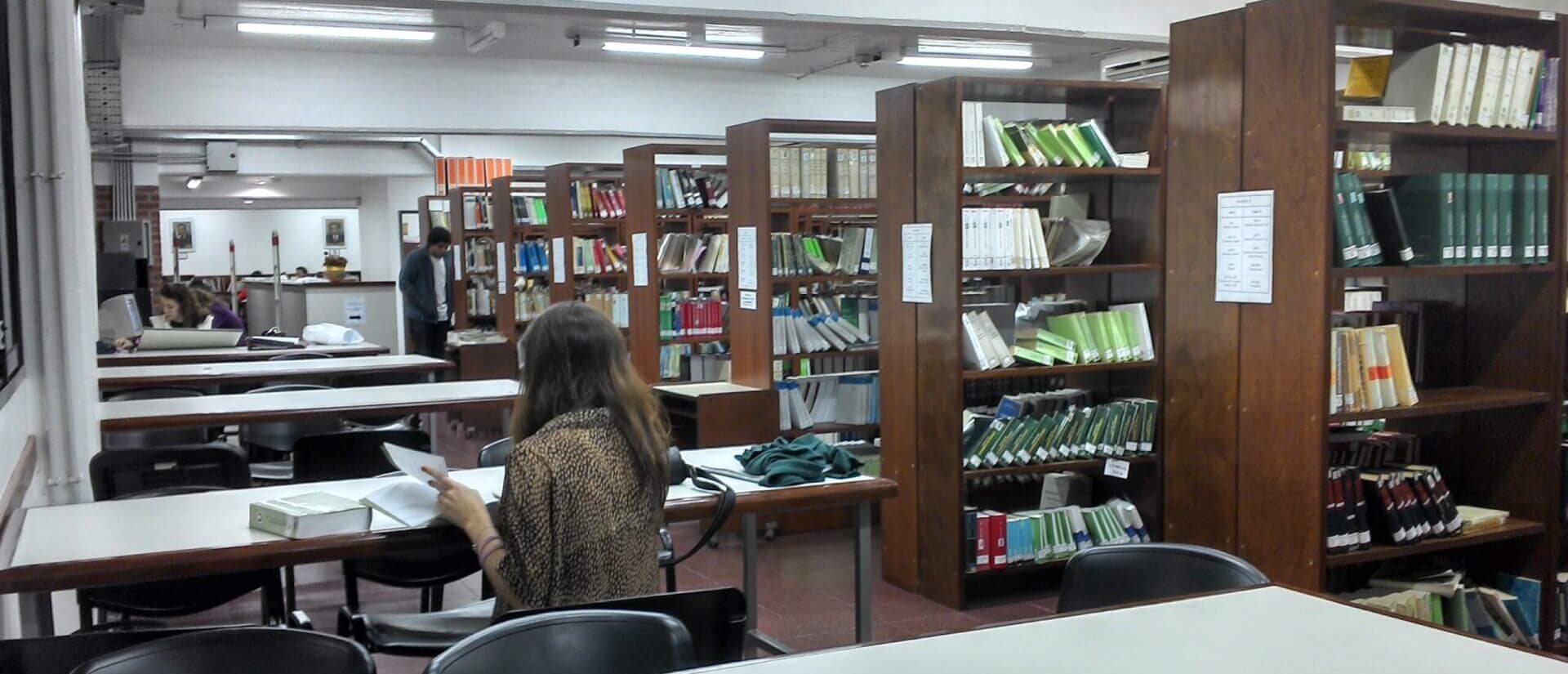 Biblioteca con estanterías, mesas de lectura y una persona estudiando
