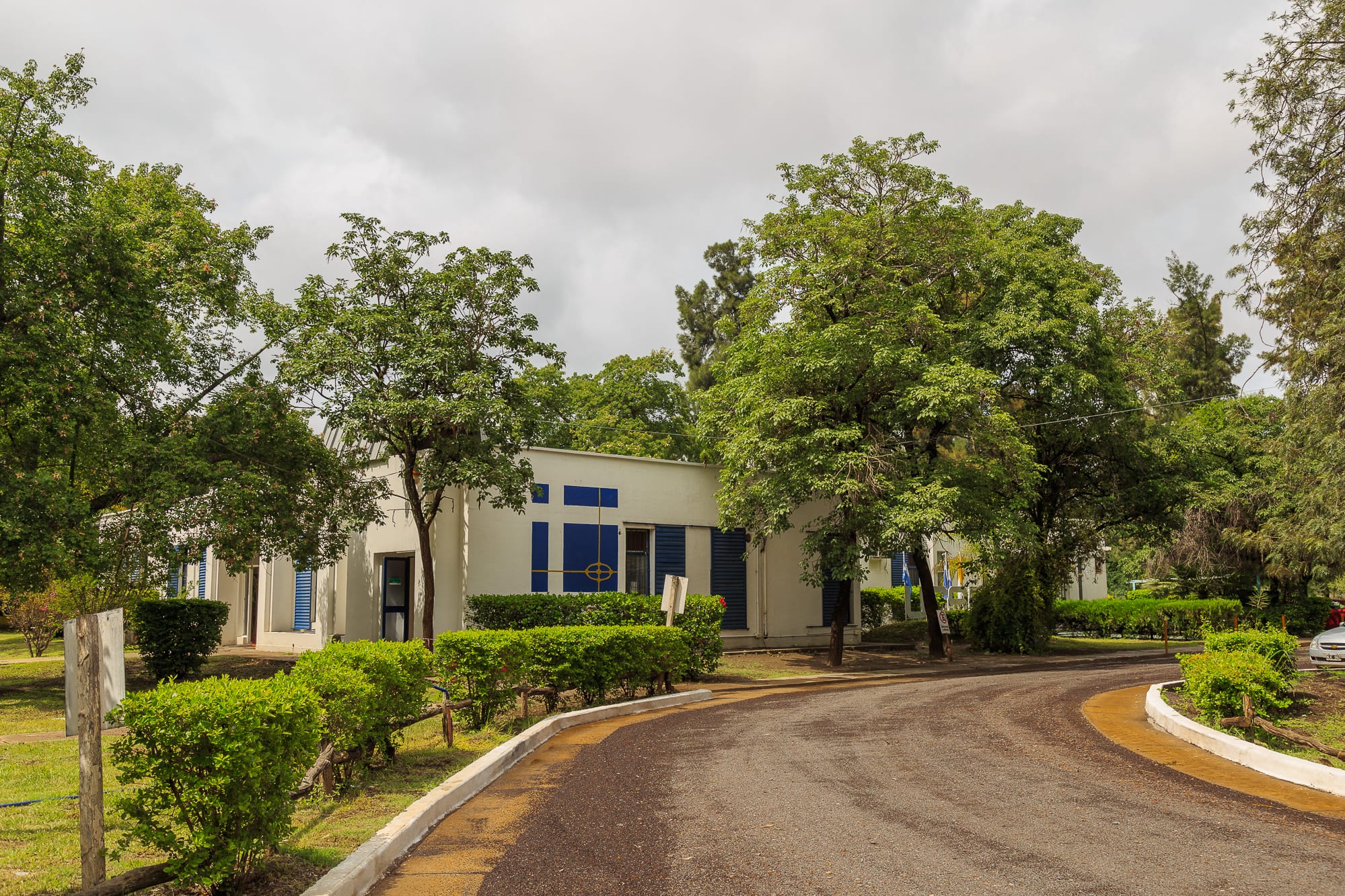 Edificio de la Universidad Católica de Santiago del Estero rodeado de árboles y jardines, con una calle interna al frente.