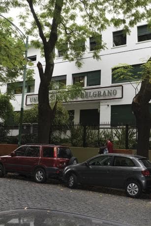 Fachada blanca de un edificio de la Universidad de Belgrano entre árboles.