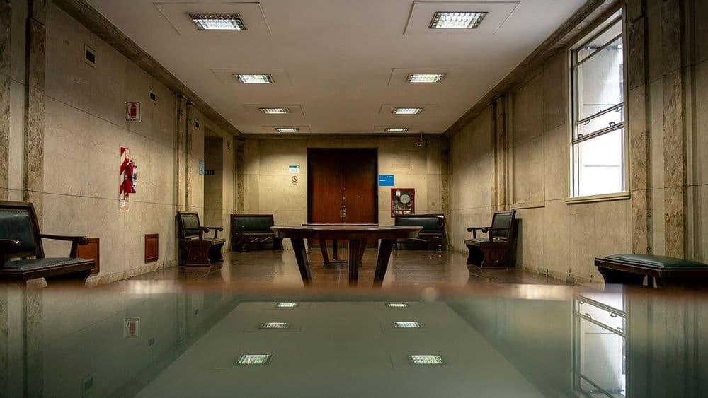 Hall interior con mesas, sillones y ventanales en un edificio de la Universidad de Buenos Aires.