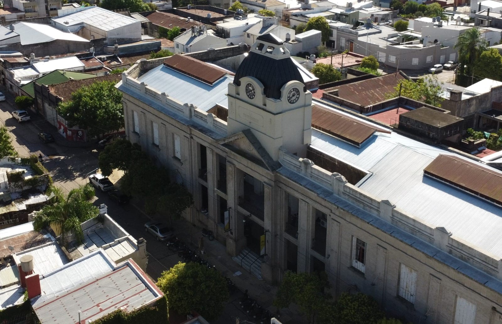Vista aérea de un edificio histórico de la Universidad de Concepción del Uruguay, con torre de reloj y galerías frontales.