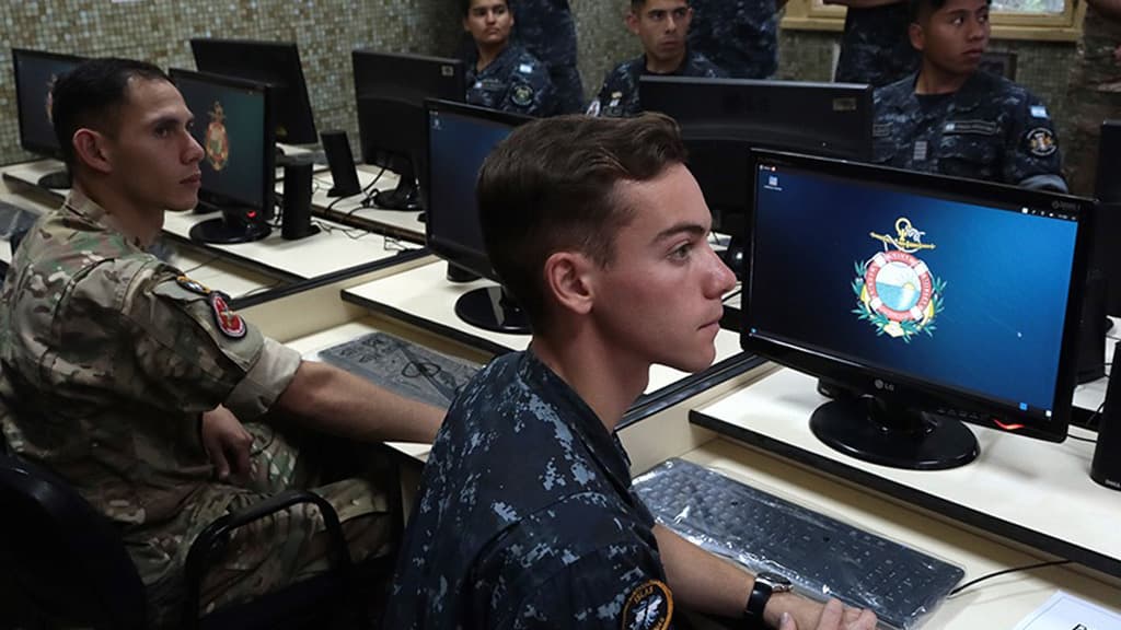 Grupo de estudiantes trabaja frente a computadoras en un laboratorio de ciberdefensa.