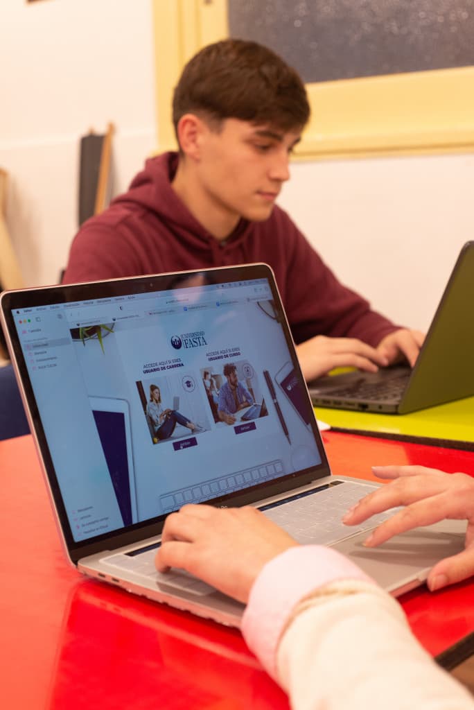Estudiantes trabajando con computadoras portátiles en una mesa de estudio.