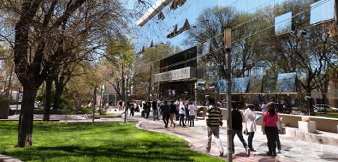 Estudiantes caminan frente a un edificio de la Universidad de Mendoza junto a un espacio verde.