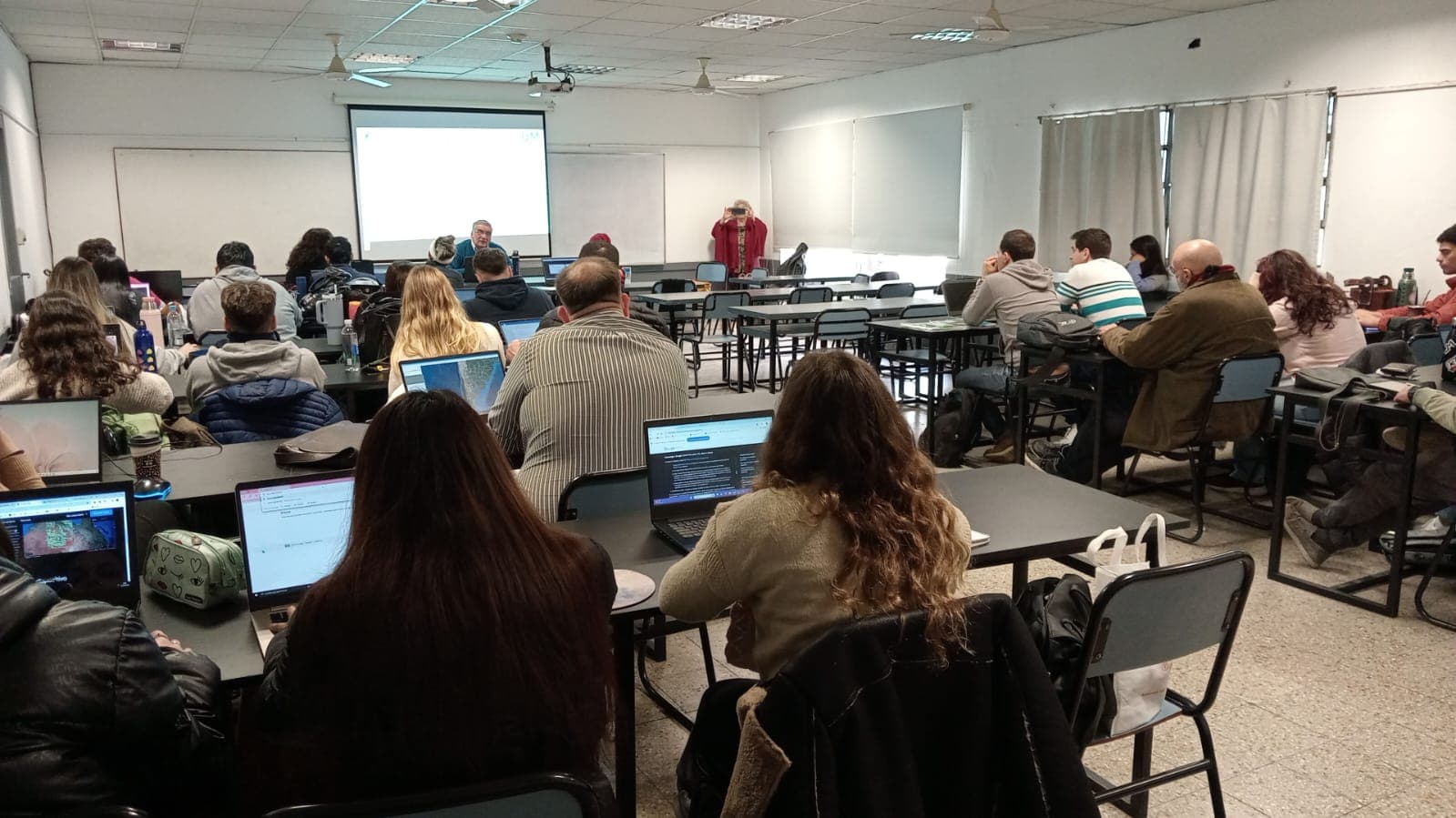 Grupo de estudiantes y docentes en un aula, con computadoras portátiles durante una clase.