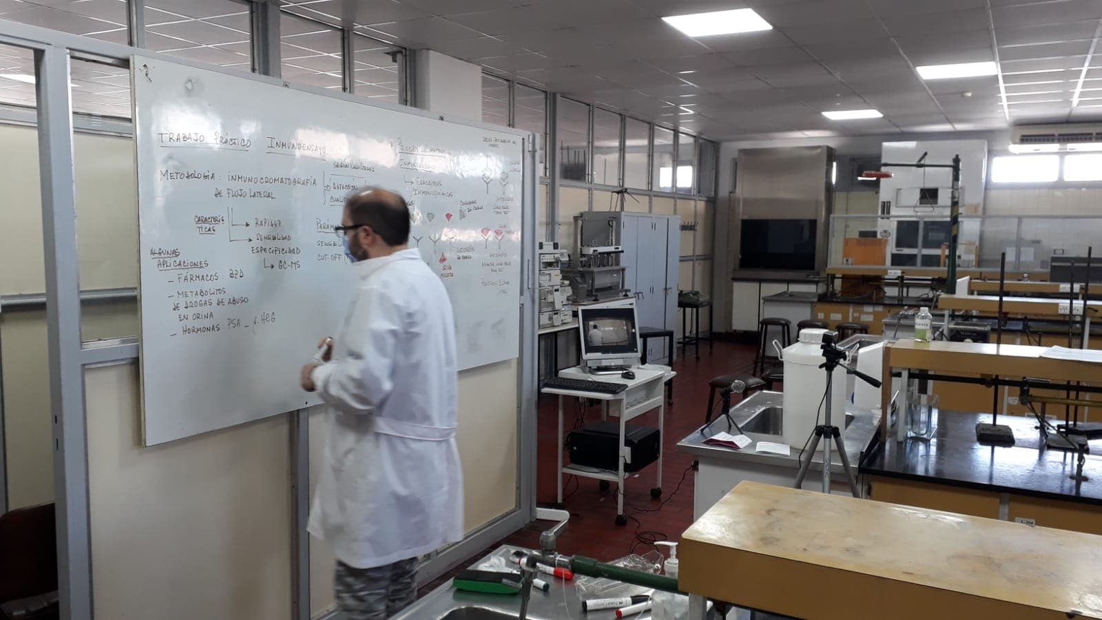 Laboratorio con mesas de trabajo, instrumental y una persona frente a un pizarrón.