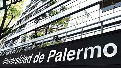 Fachada de la Universidad de Palermo con ventanales y árboles en primer plano.
