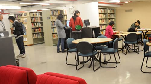 Sala de lectura de biblioteca con estanterías, mesas y personas estudiando.