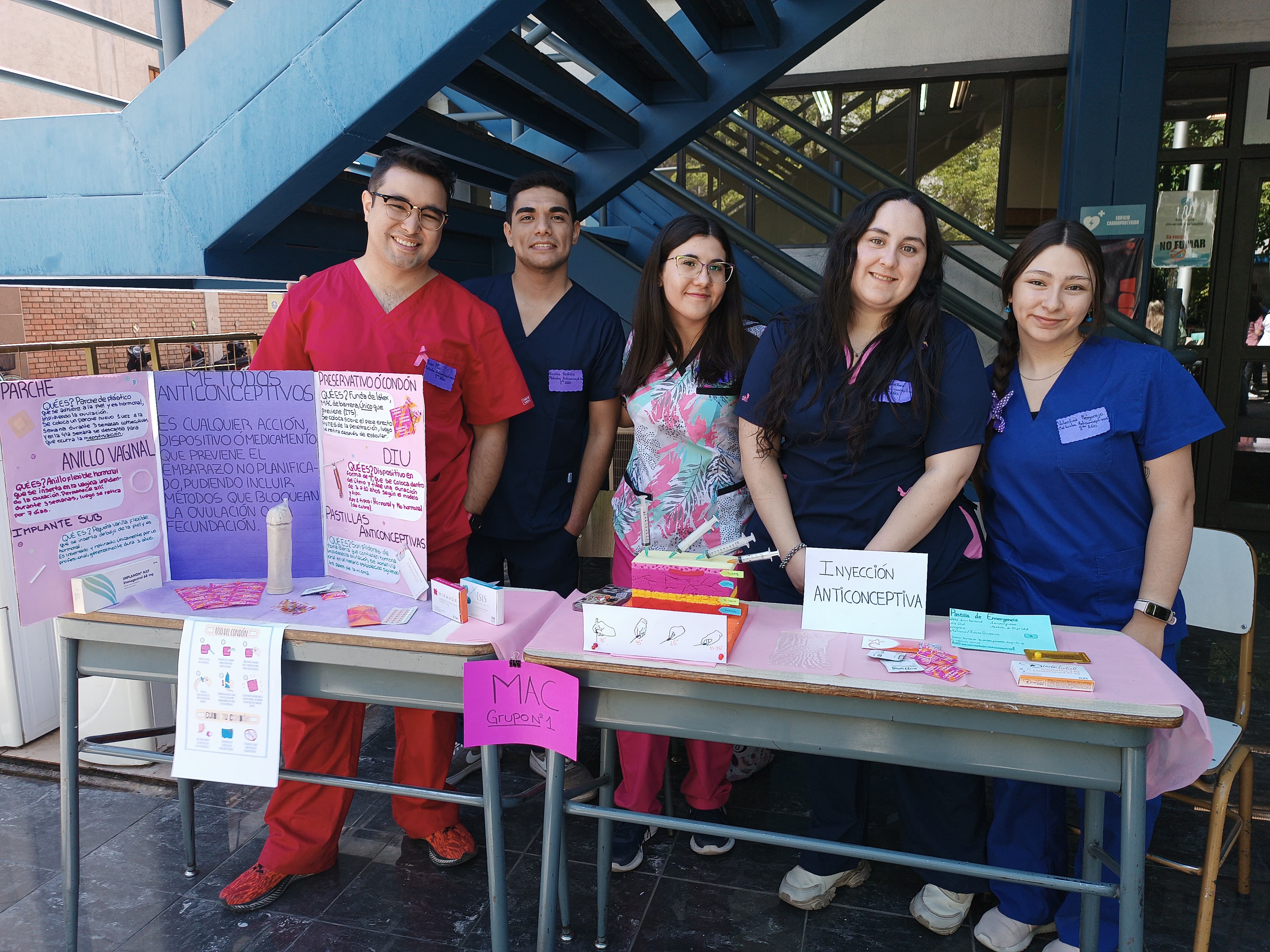 Grupo de estudiantes de obstetricia junto a una mesa informativa en un espacio exterior universitario.