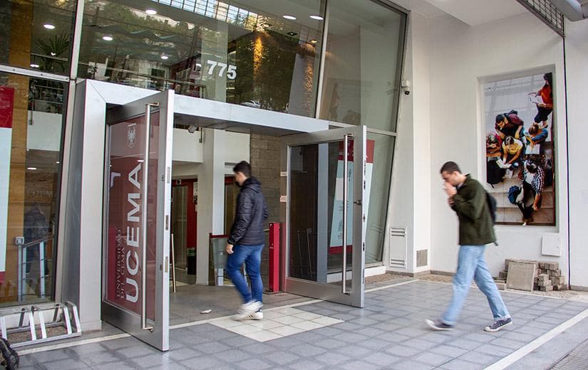 Entrada vidriada de una sede de UCEMA con señalética institucional vertical y personas ingresando.