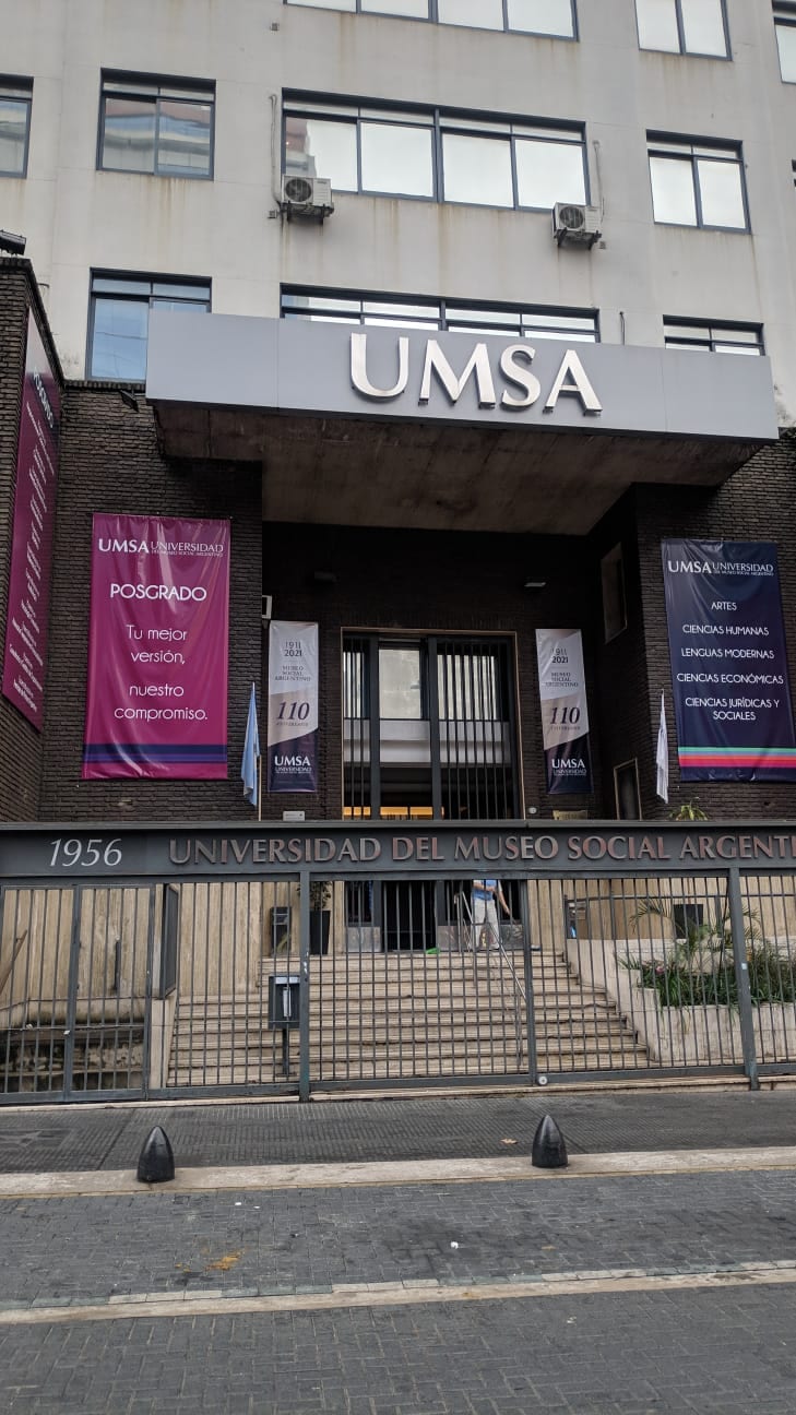 Entrada de la sede central de UMSA, con marquesina institucional y acceso sobre la vereda.