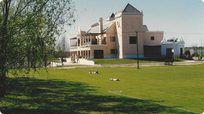 Edificio de la universidad junto a un amplio jardín con césped y árboles.