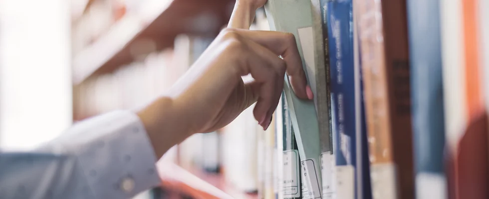 Mano tomando un libro de una estantería con otros volúmenes al fondo