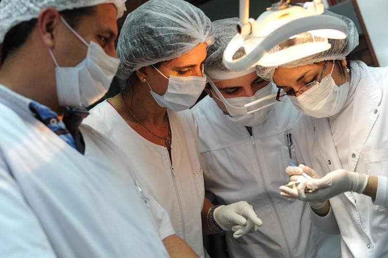 Estudiantes con indumentaria de laboratorio realizan una práctica con instrumental.