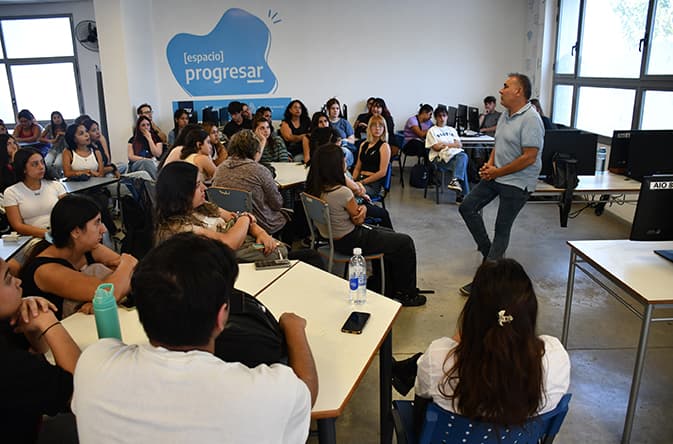 Clase con estudiantes sentados mientras un docente expone frente al aula.