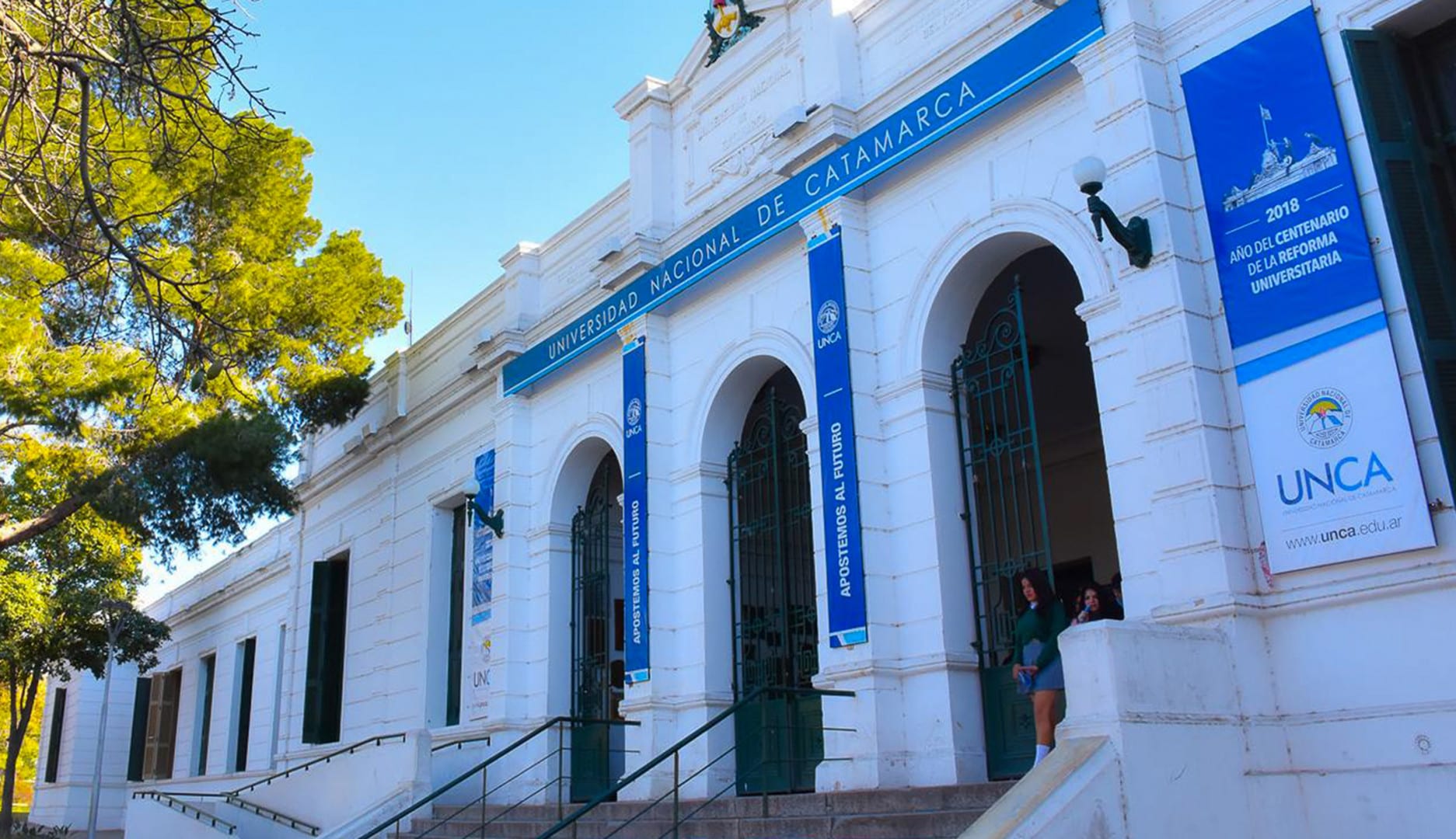 Fachada de la Universidad Nacional de Catamarca con arcos de entrada y cartelería institucional.