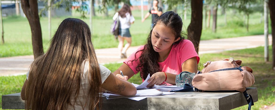Estudiantes trabajando con apuntes en una mesa al aire libre.