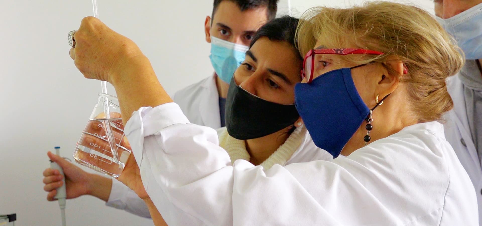 Personas con guardapolvo observan una práctica con material de laboratorio.