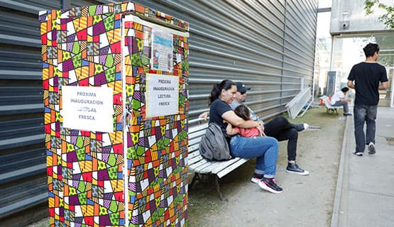 Personas sentadas junto a una biblioteca comunitaria decorada, en un espacio exterior del campus.