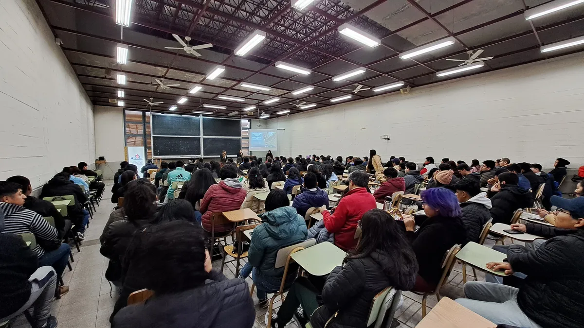Vista amplia de un aula universitaria con estudiantes sentados durante una charla.