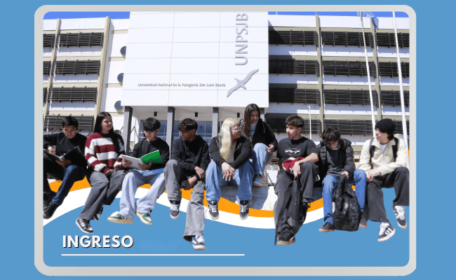 Estudiantes sentados frente a un edificio identificado con las siglas UNPSJB.