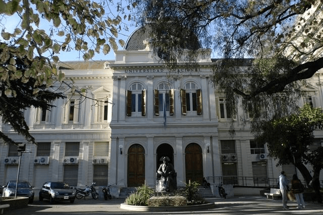 Fachada de un edificio de la Universidad Nacional de La Plata, vista desde la calle entre árboles.