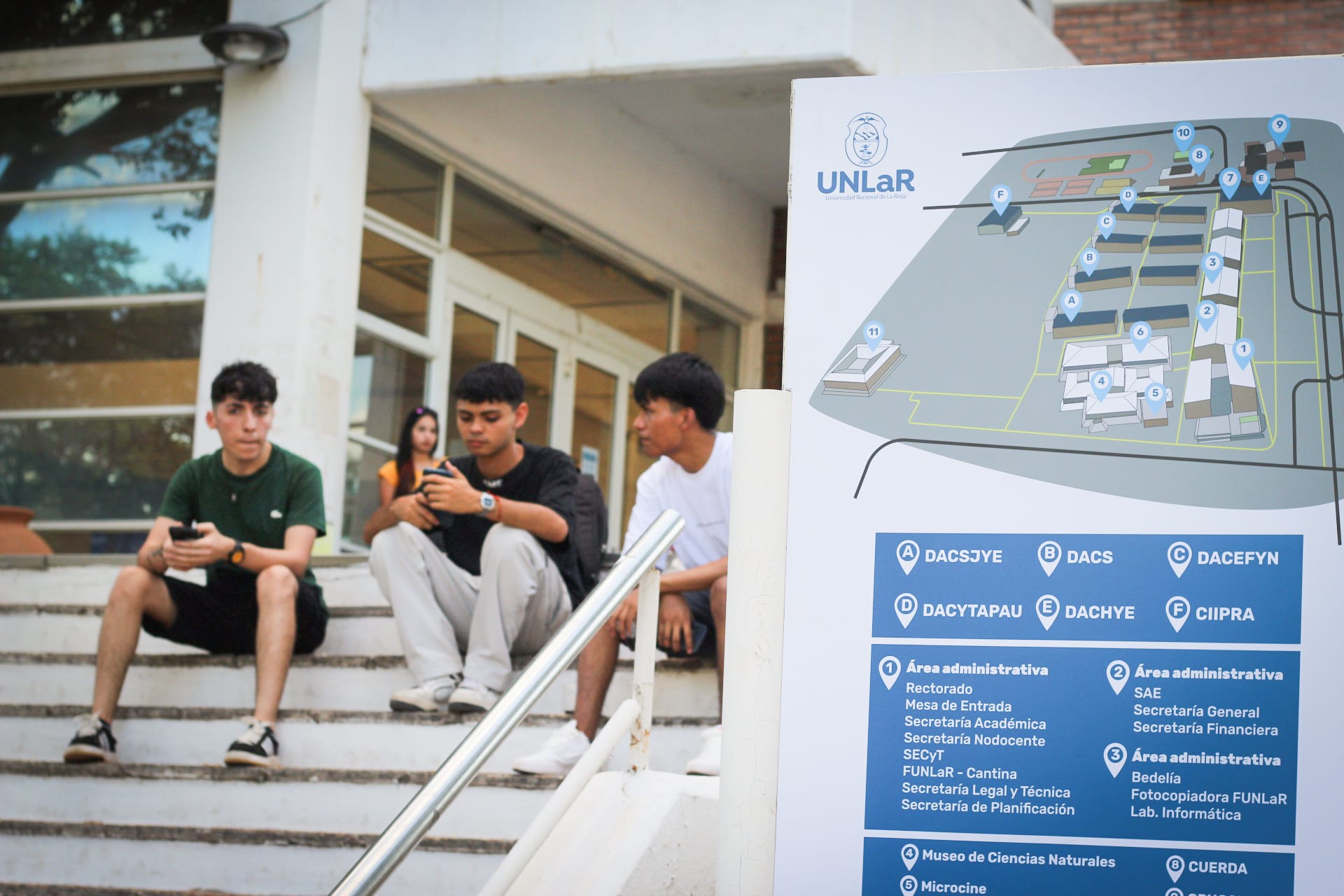 Estudiantes sentados en las escaleras junto a un plano del campus de la UNLaR