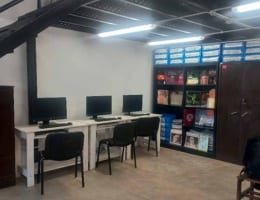 Sala interior con computadoras de escritorio, sillas y estanterías.
