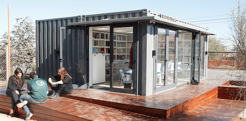 Biblioteca en un módulo vidriado, con estanterías y estudiantes sentados en la plataforma exterior.